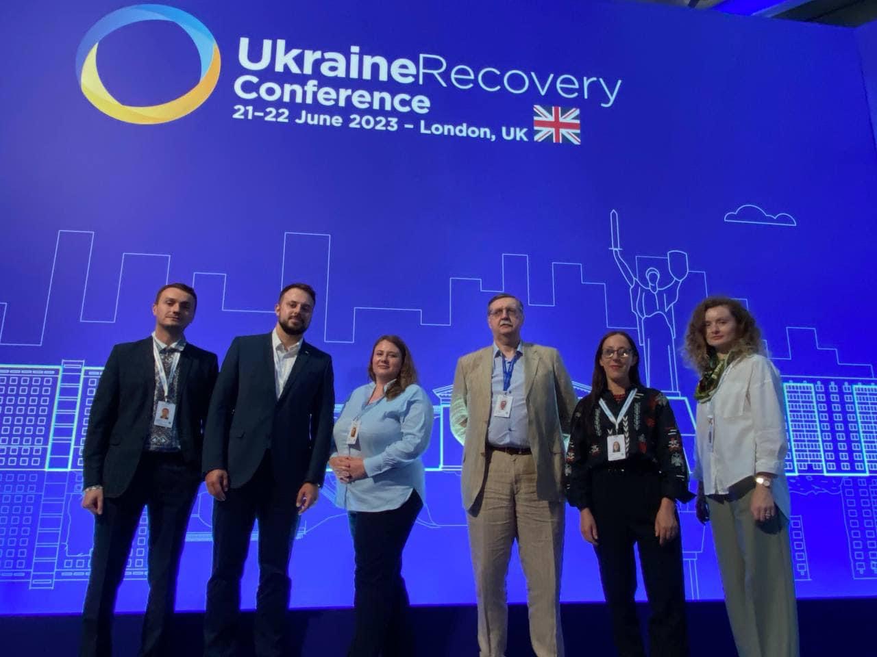 Група людей стоїть на тлі сцени з написом "Ukraine Recovery Conference 2023".