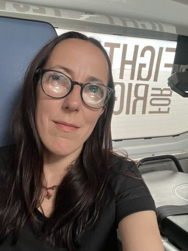 Юлія в окулярах, має темне довге волосся, одягнена у чорну футболку. Вона сидить в авто Fight For Right.