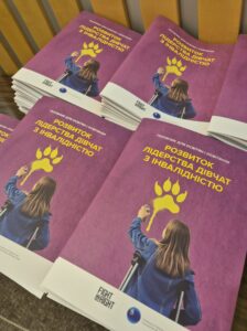 На фото кілька стосів посібника "Розвиток лідерства дівчат з інвалідністю" із темнорожевою обкладинкою.