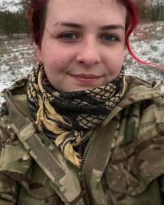 На селфі усміхнена військова з волоссям темно-рожевого кольору, вона в хустці-арафатці бежево-чорній у клітинку навколо шиї і камуфляжній куртці (кольори мультикам). Це Катерина Поліщук, наша Пташка, яка пройшла полон і нині допомагає звільняти Україну від російських окупантів.