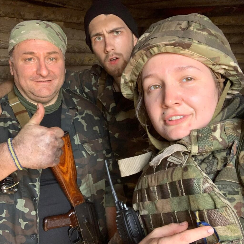 На фото три людини. Справа в шоломі і в плитоносці з рацією Катерина Приймак, ветеранка. За нею два чоловіки теж у формі кольору мультикам, молодого і середнього віку. Той чоловік що зліва тримає руку перед собою і показує великим пальцем вгору - "чудово"