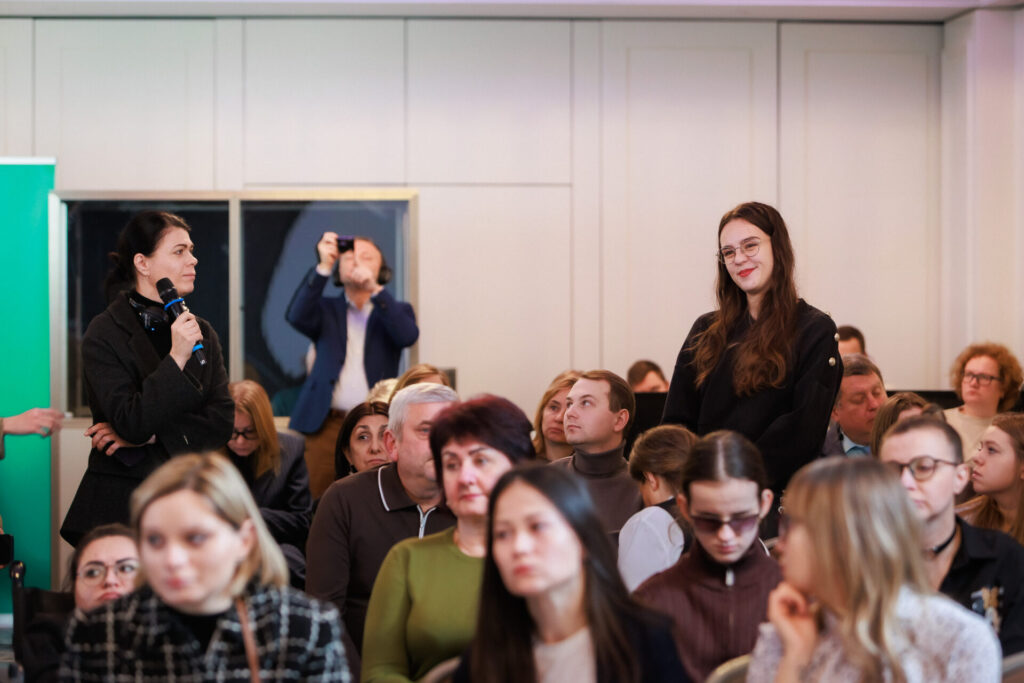 Учасники та учасниці Конференції, загальне фото присутніх у залі. Стоїть Іванна Михайленко, голова ГО Світ тиші і задає запитання спікерам та спікеркам, а лівіше Ірина Тернова пере 